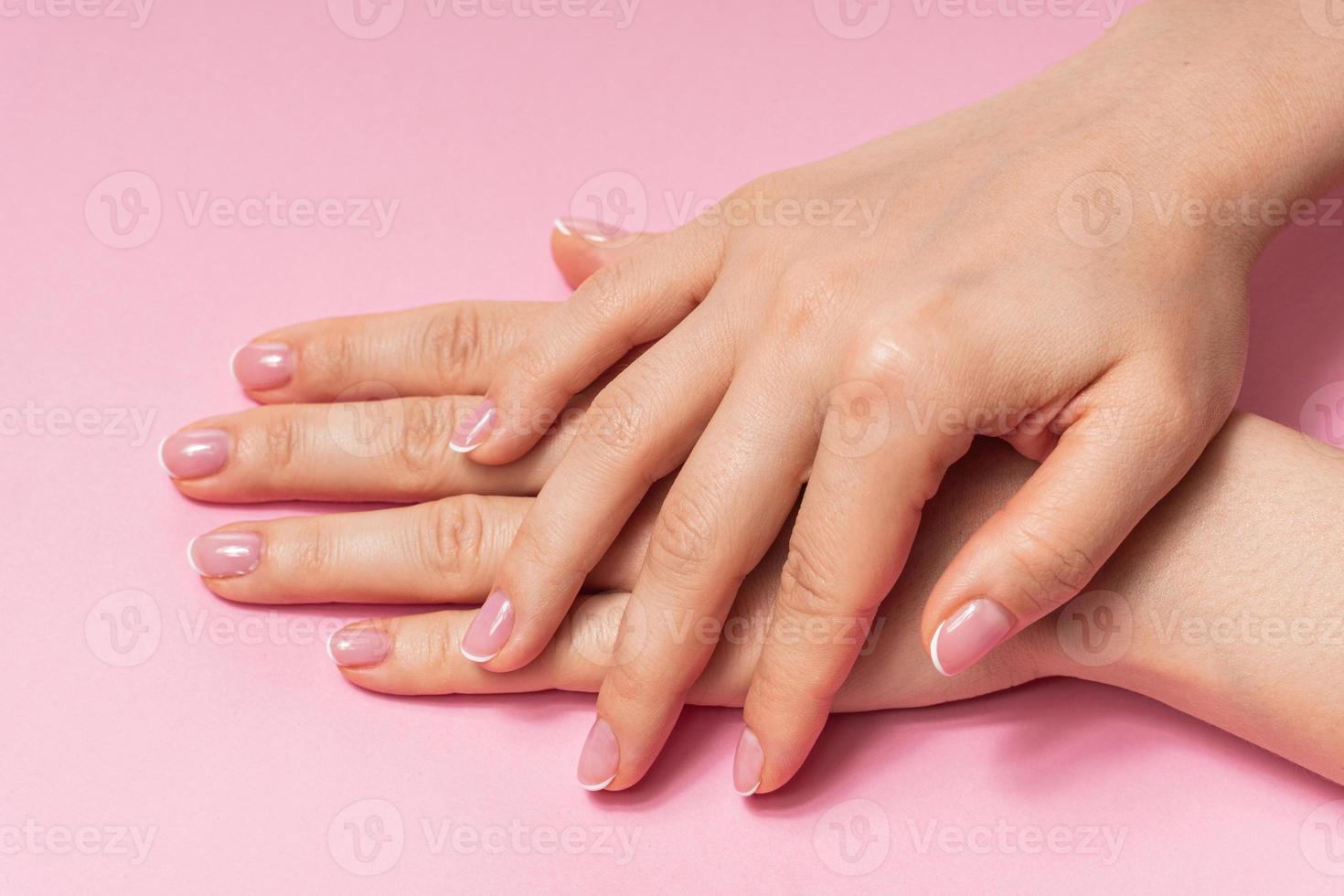 Female hands with soft skin and beautiful french manicure against pink background photo