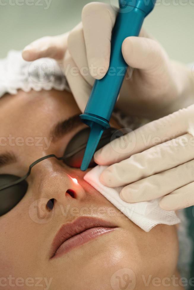 Woman during laser mole removal in a medical aesthetic clinic photo