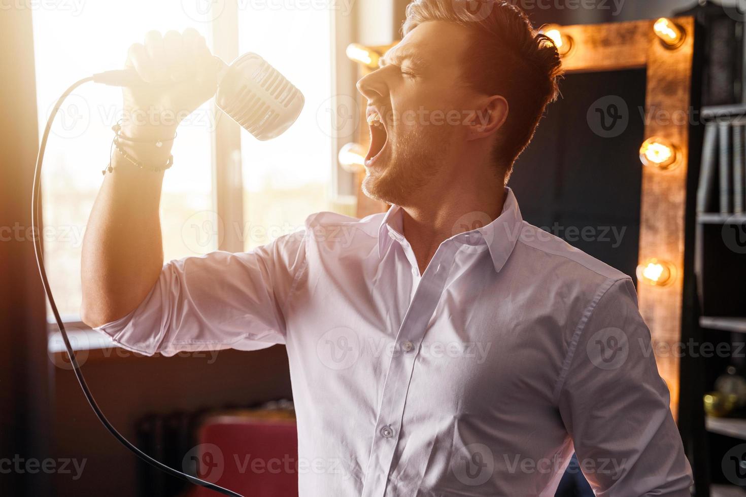 Young man with microphone is singing loudly at home photo