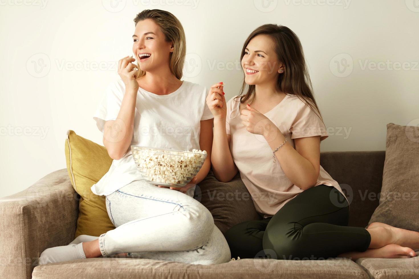 Two beautiful girlfriends watching tv show and eating popcorn photo