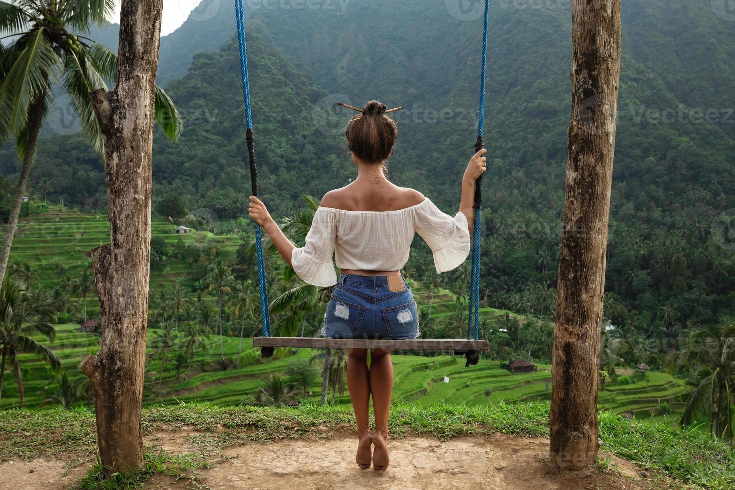 mujer en columpios de cuerda con hermosas vistas a las terrazas de arroz en bali. foto