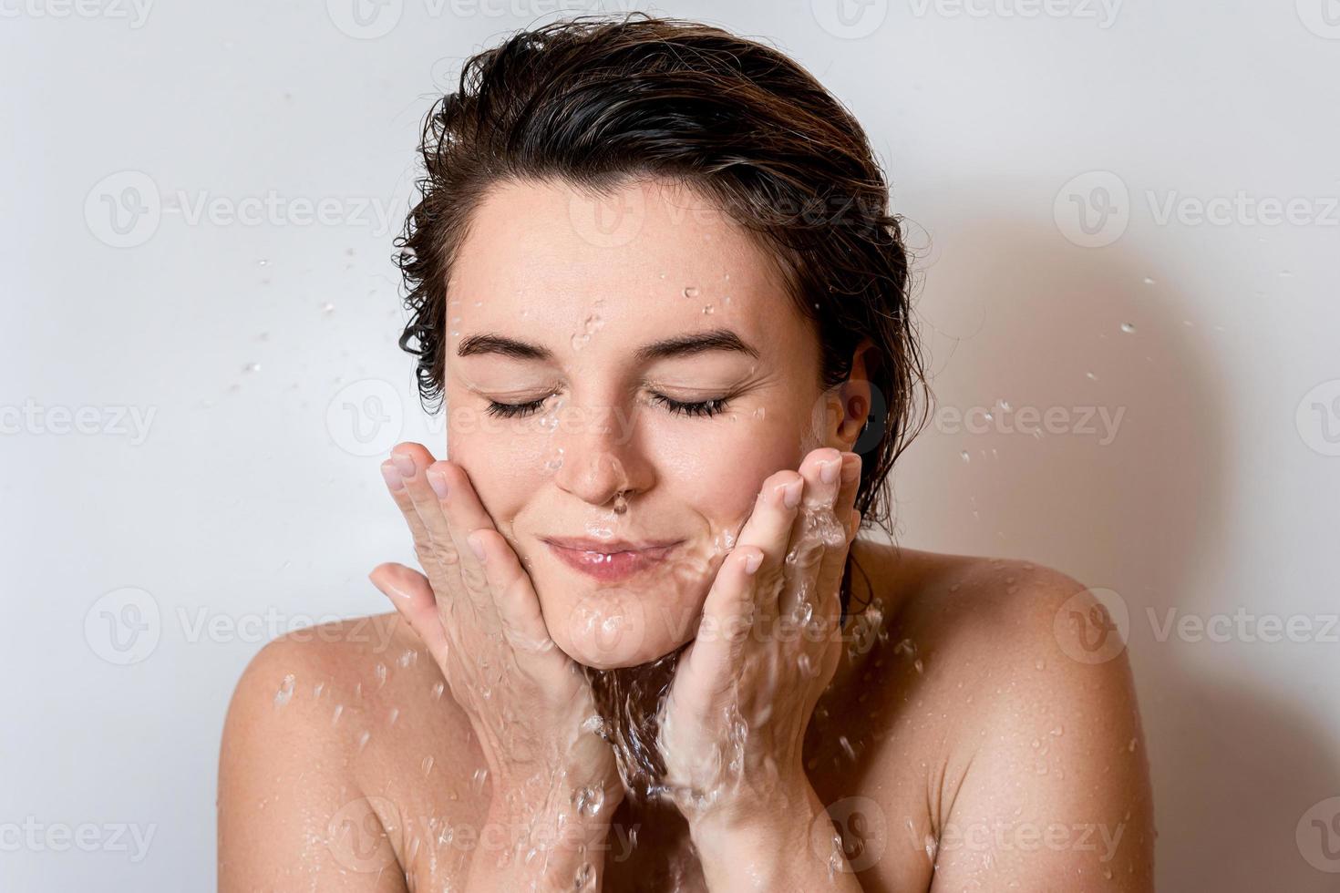 mujer joven lavándose la cara con agua limpia foto