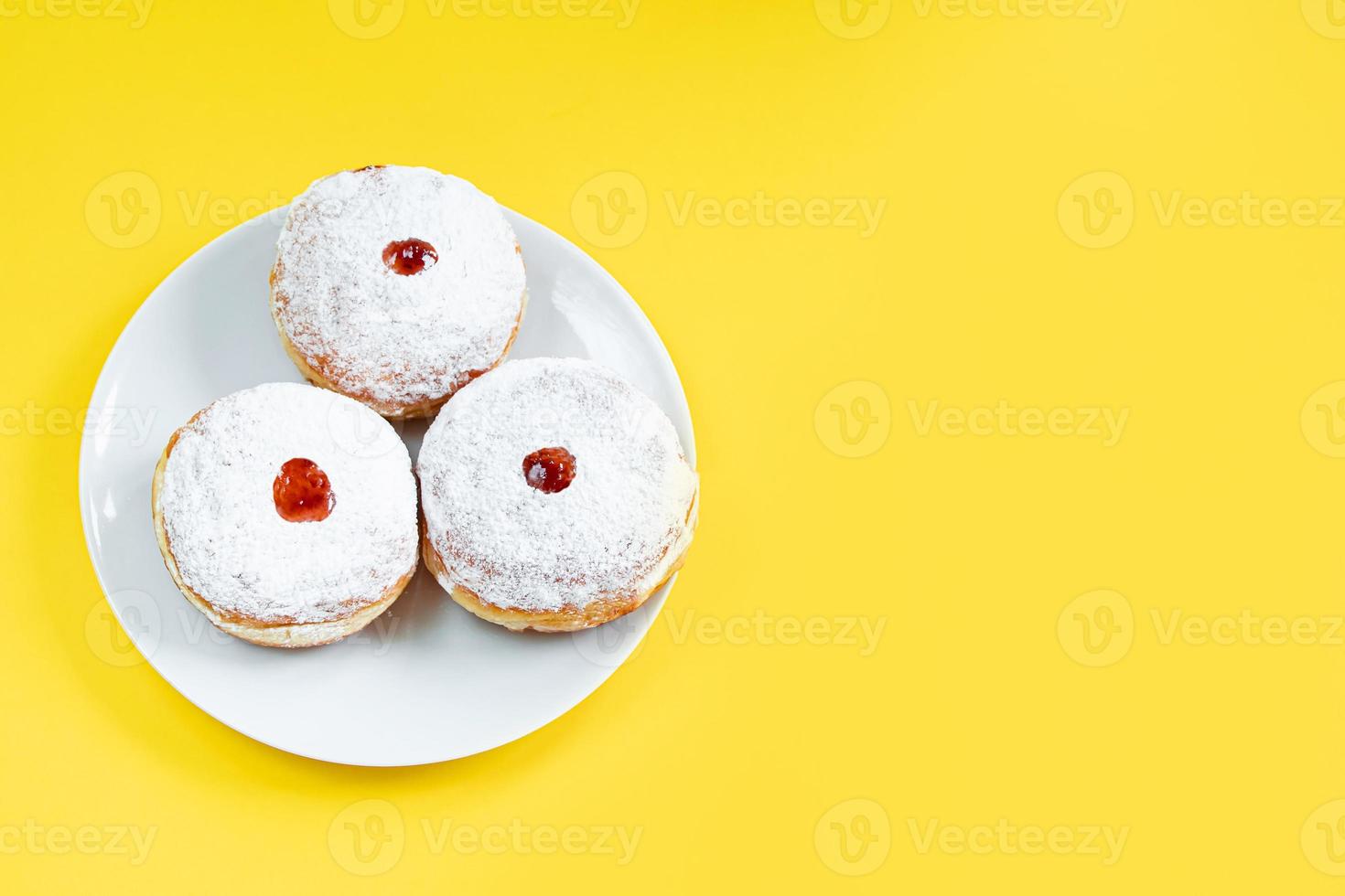 Plate with traditional Jewish dessert Sufganiyot on yellow background. Celebrating religious Judaism holiday. Donuts with jam and powdered sugar. photo