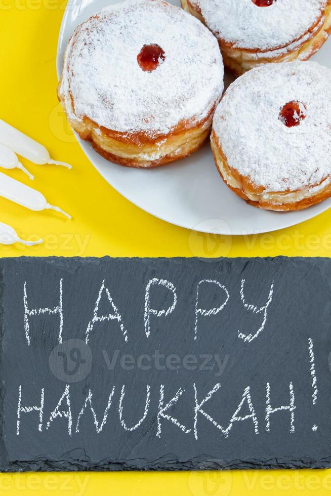 Happy Hanukkah. Jewish dessert Sufganiyot on yellow background. Symbols of religious Judaism holiday. Donuts, candles and gift. photo