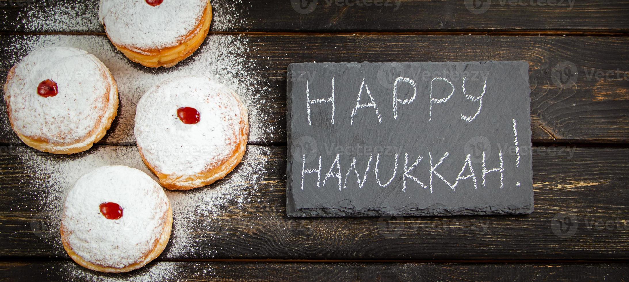 feliz Jánuca. postre tradicional sufganiyot sobre fondo de madera oscura. donuts, velas y regalos. celebrando la festividad judía. foto