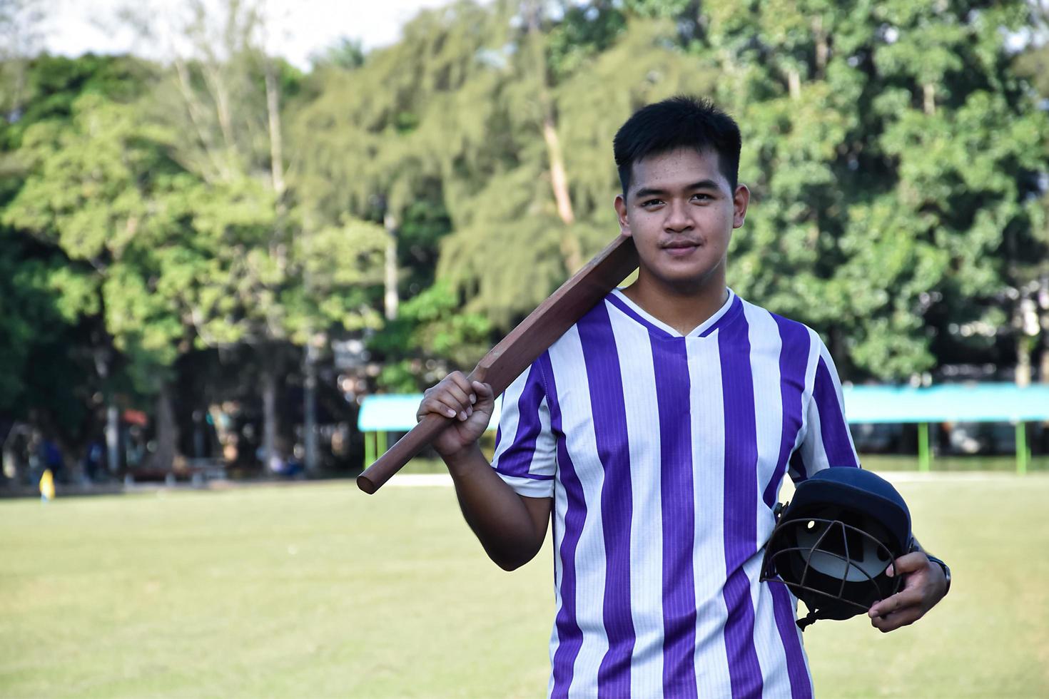 Male cricket coach holds helmet and bat in the green grass court of school before teaching cricket sport to students at school in the afternoon of the day. photo