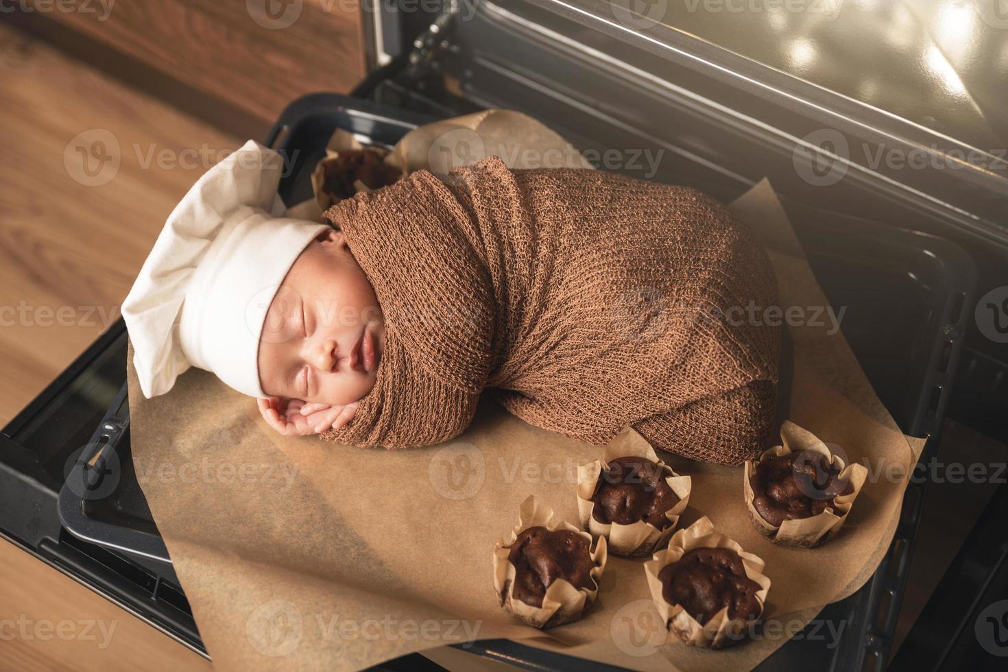 un bebé recién nacido con sombrero de chef está tirado en la bandeja del horno con muffins foto