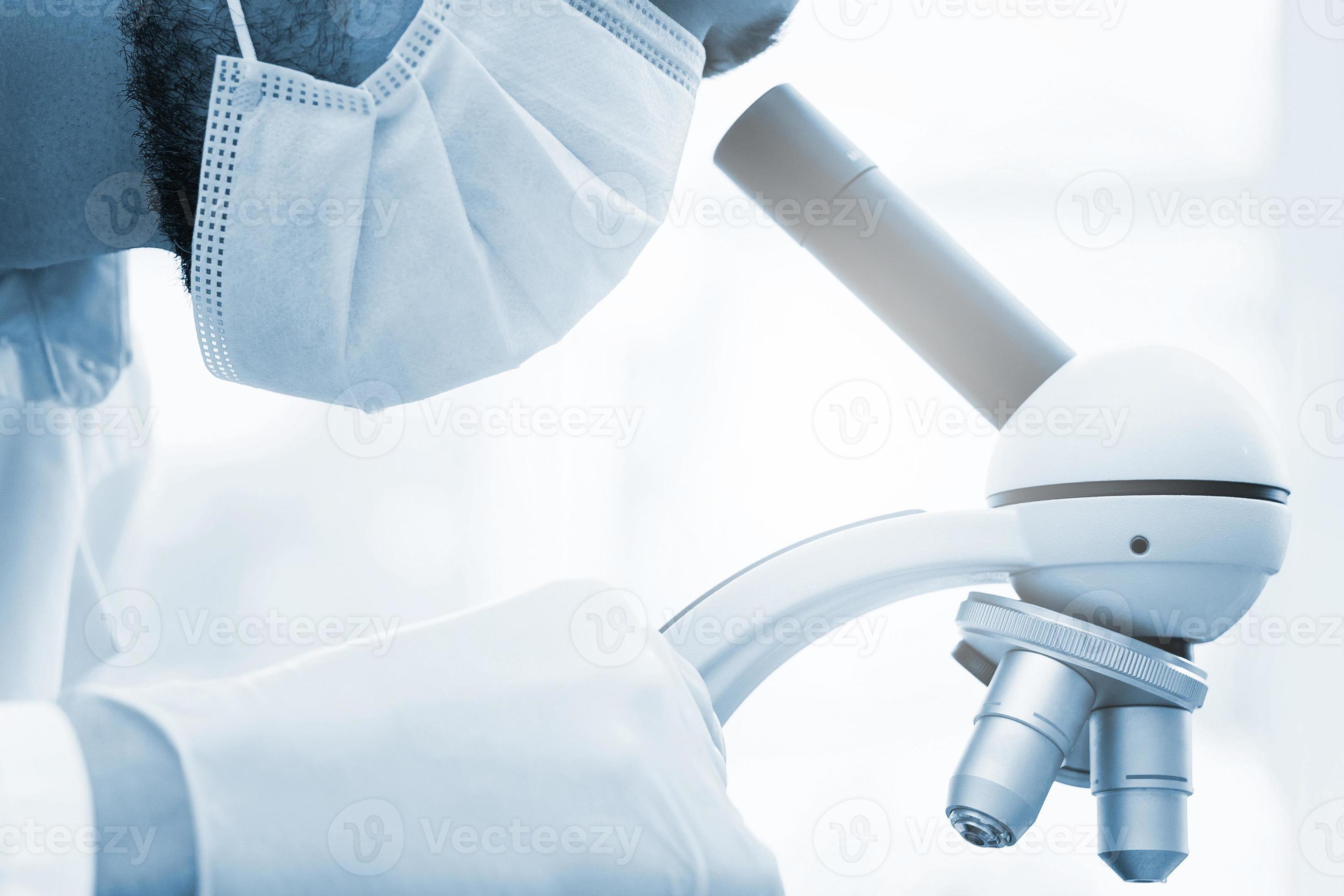 el científico que usa una máscara médica está usando un microscopio en