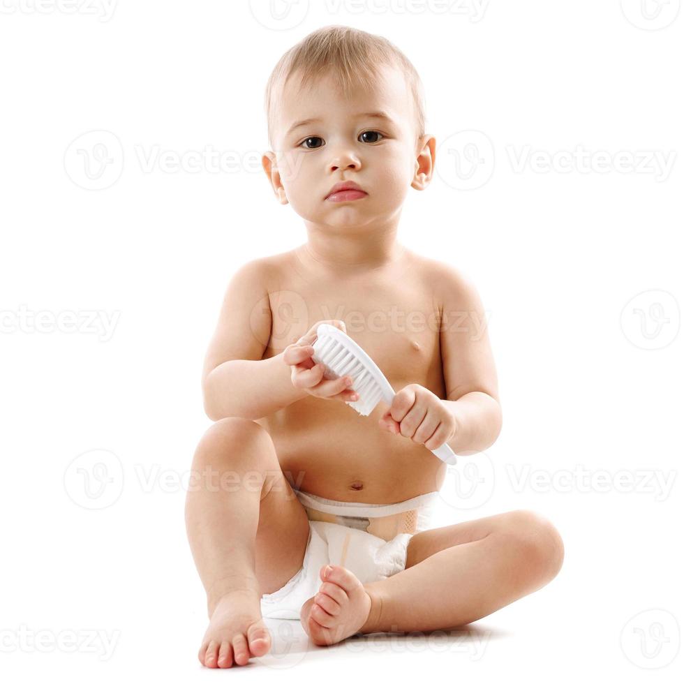 niño pequeño en pañales sentado y jugando con cepillo. foto