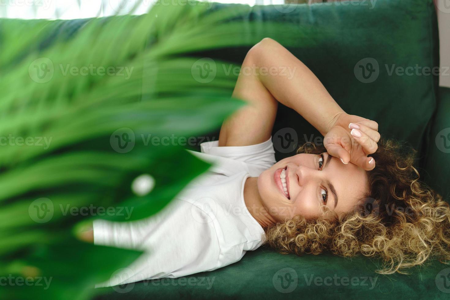 Beautiful woman with curly hair lying on green sofa photo