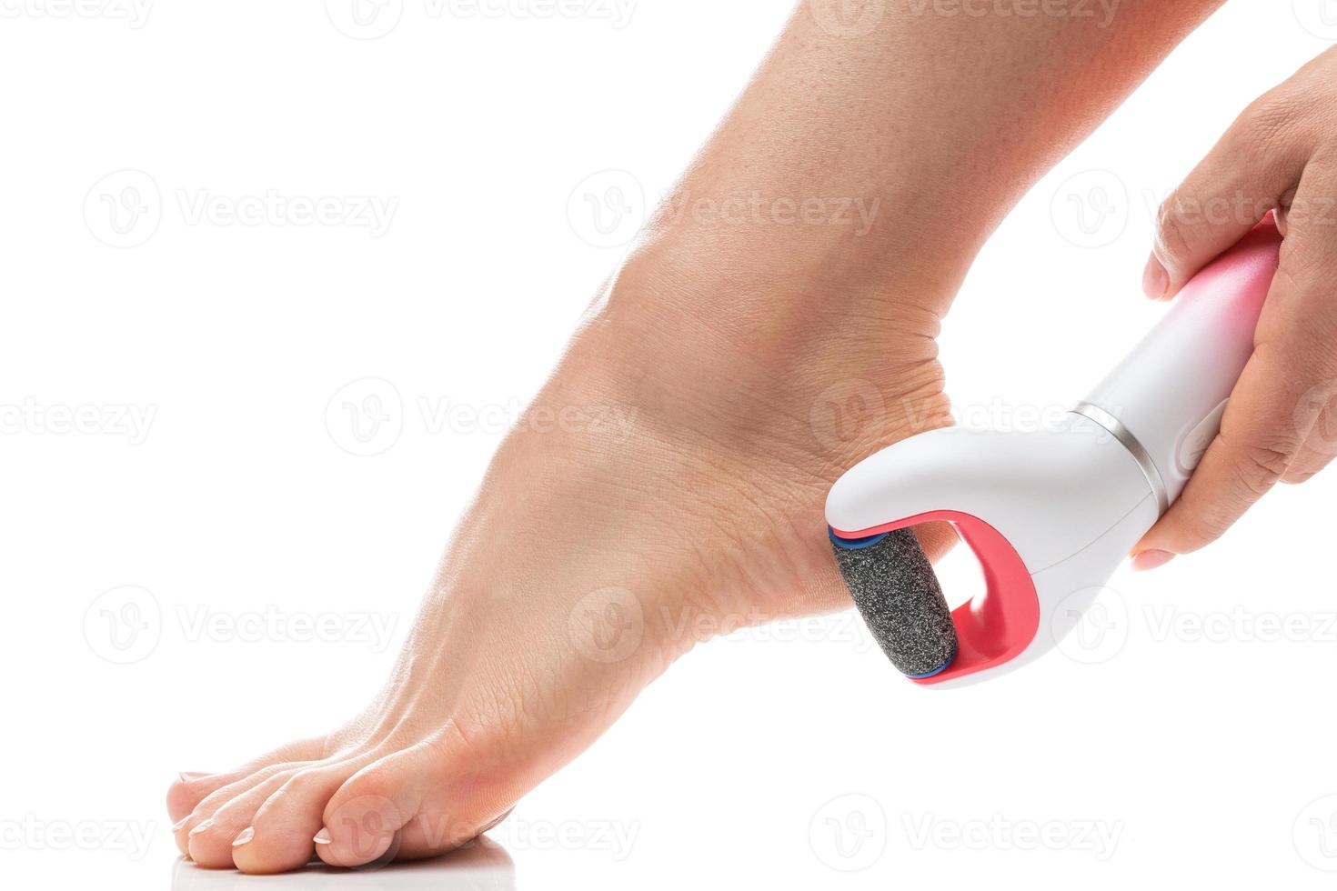 pies femeninos y lima eléctrica para pies para eliminación de callos y piel muerta sobre fondo blanco foto