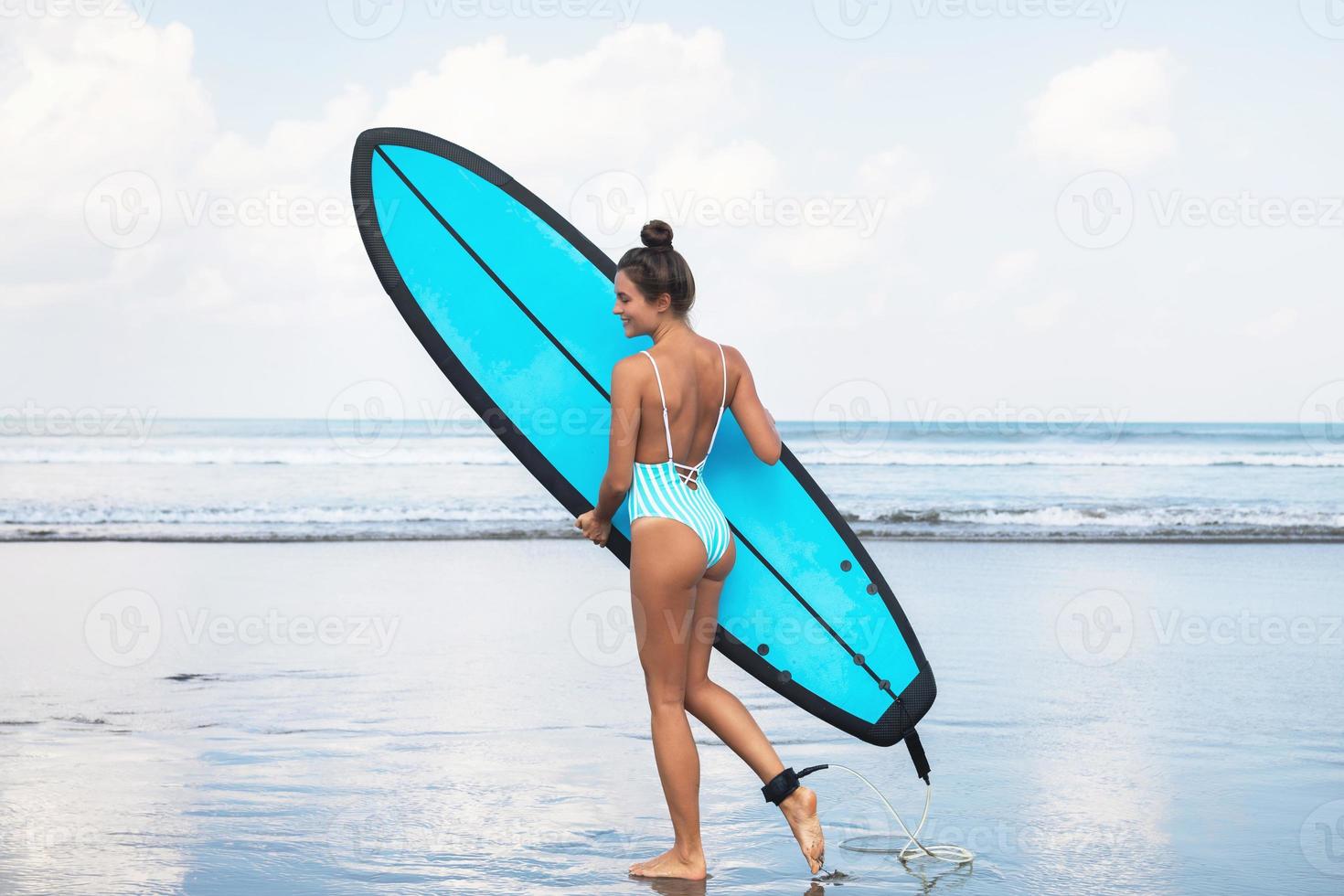 mujer joven con traje de baño a rayas con tabla de surf en la playa foto