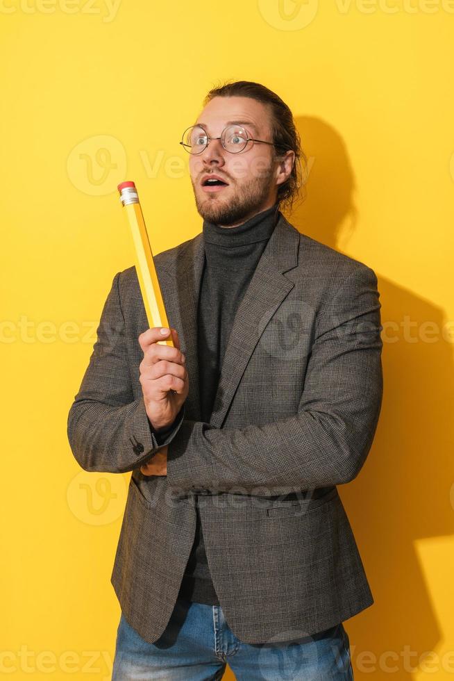 Inspired man wearing glasses holding big pencil on yellow background photo