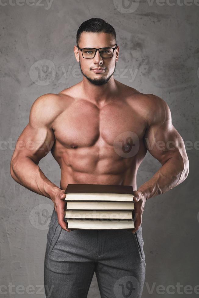 Smart and muscular man with a heap of books photo