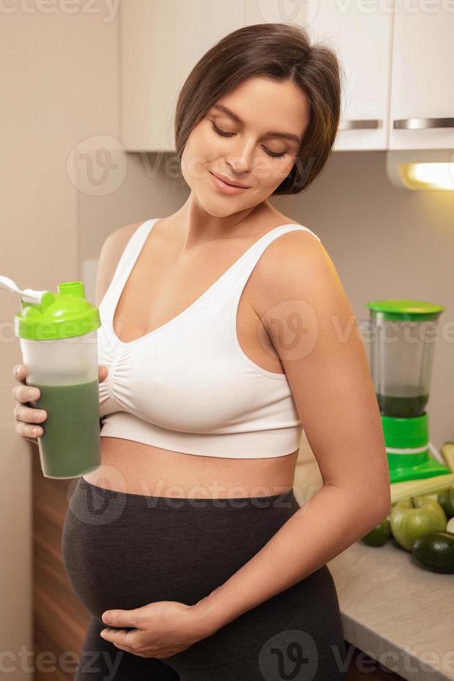 mujer embarazada sosteniendo un agitador con un cóctel de proteína verde foto