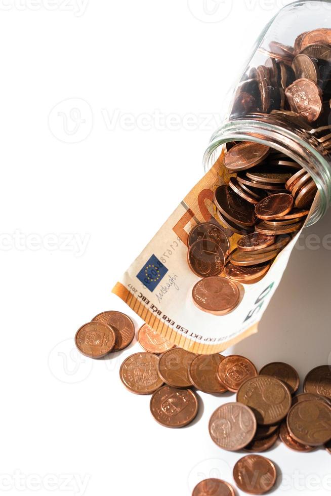 Billete de cincuenta euros y monedas de bajo valor de cobre brillante derramadas de un frasco de vidrio. foto