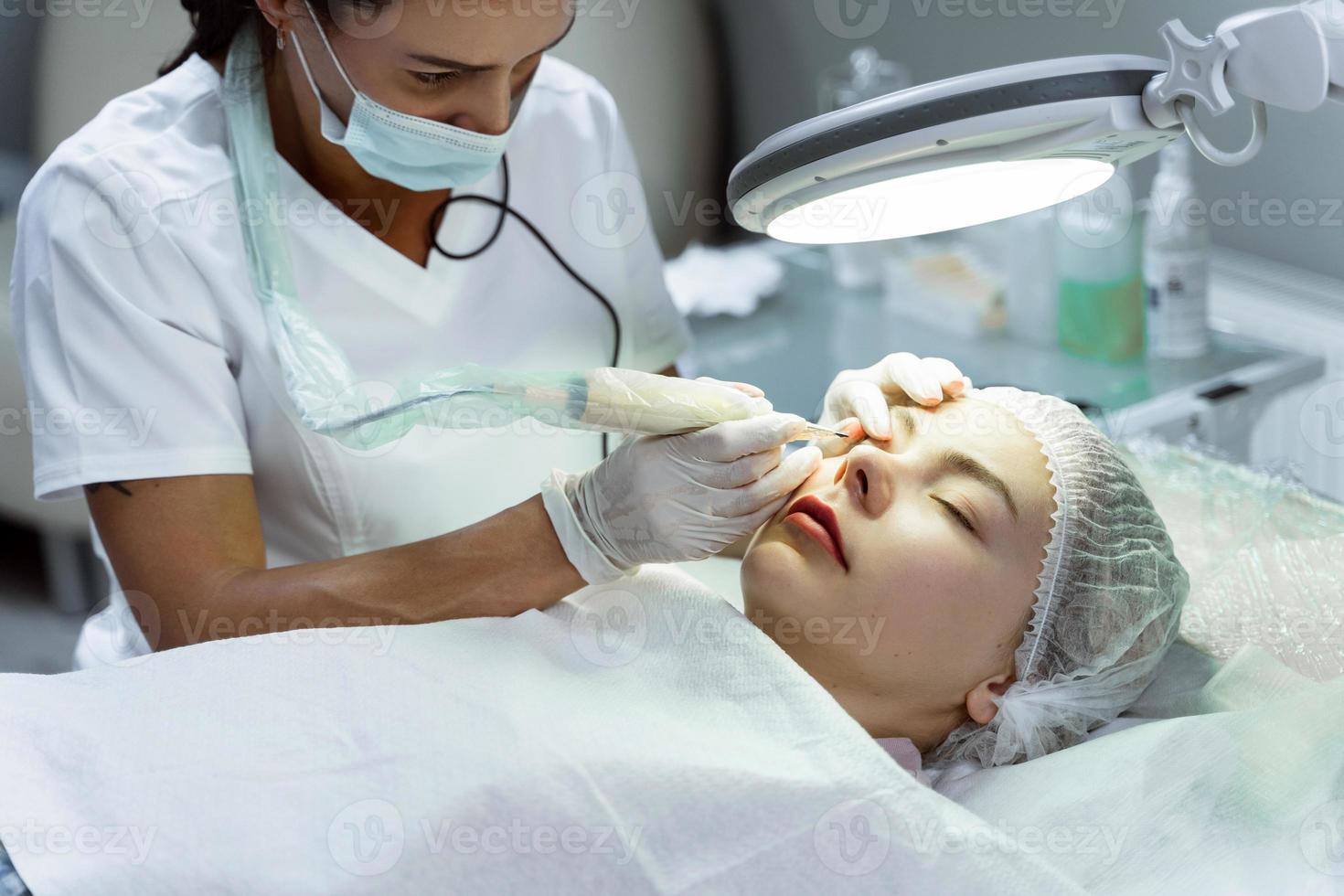 Permanent makeup artist and her client during lash line enhancement treatment photo