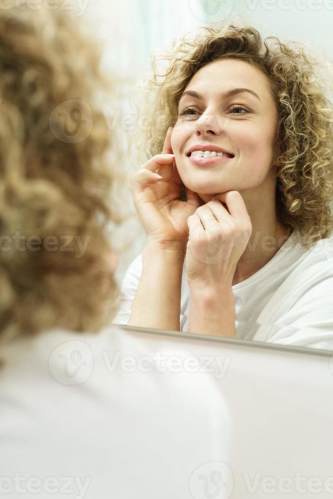 Beautiful woman with curly hair looking into the mirror in a bathroom photo