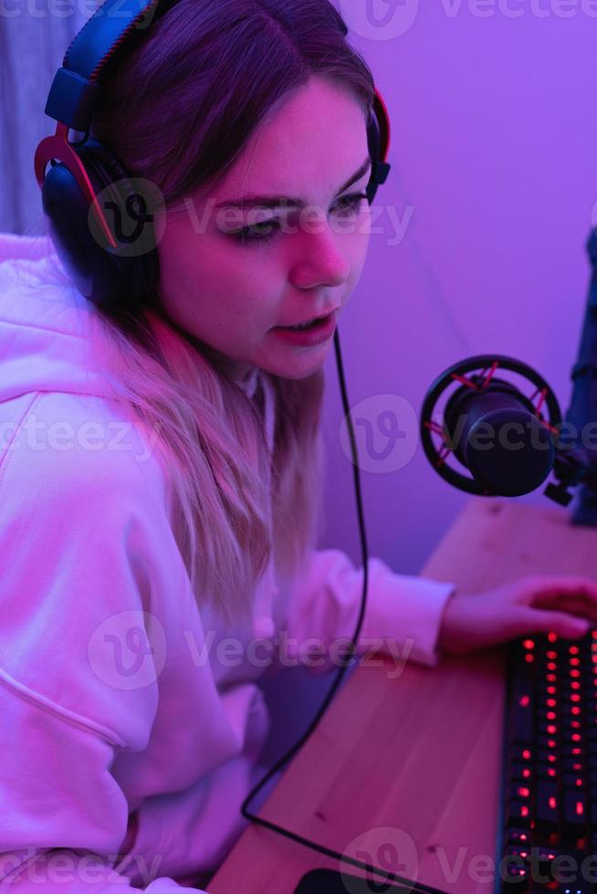 Woman blogger using condenser microphone during online podcast in room with neon light photo