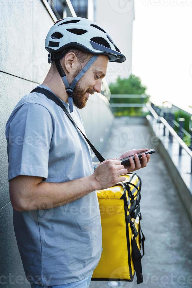 Express food delivery courier with insulated bag looking at phone. photo