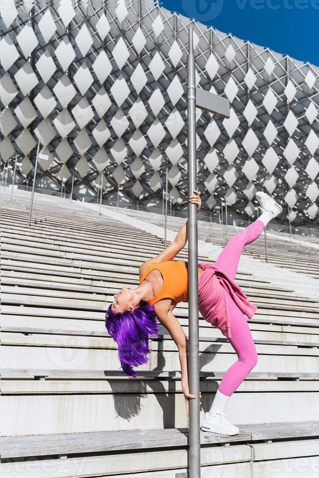Carefree woman dancer wearing colorful sportswear having fun on the pole photo