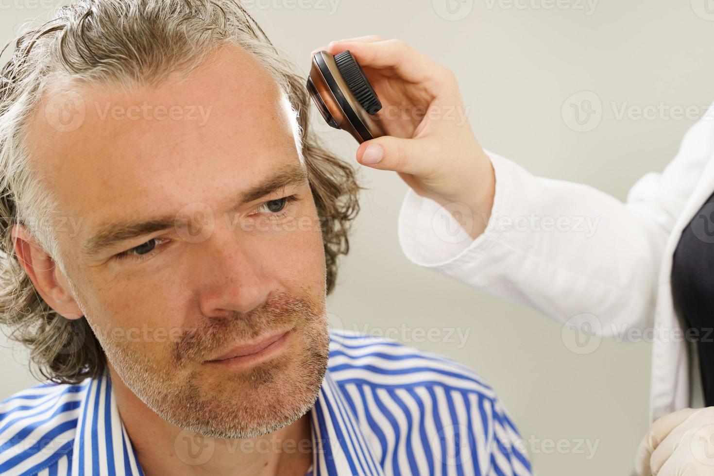 Dermatologist is using dermatoscope for facial skin examination. photo