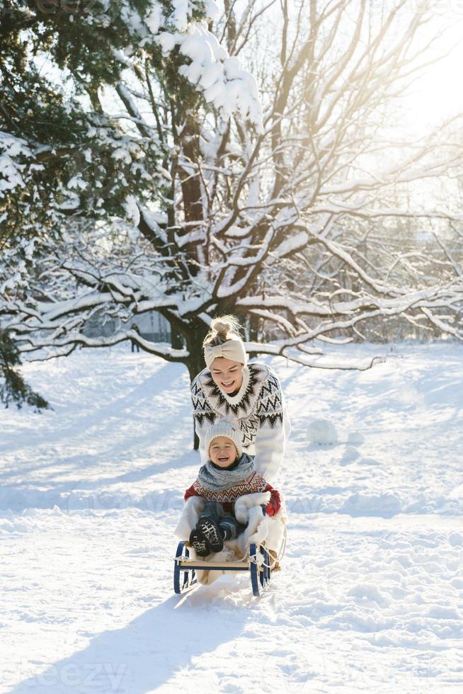 Mother and her cute little son having on a sledding hill during sunny winter day photo