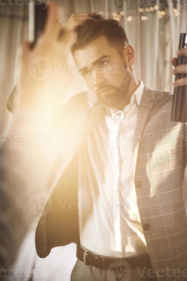 Handsome and bearded man is using hairspray photo