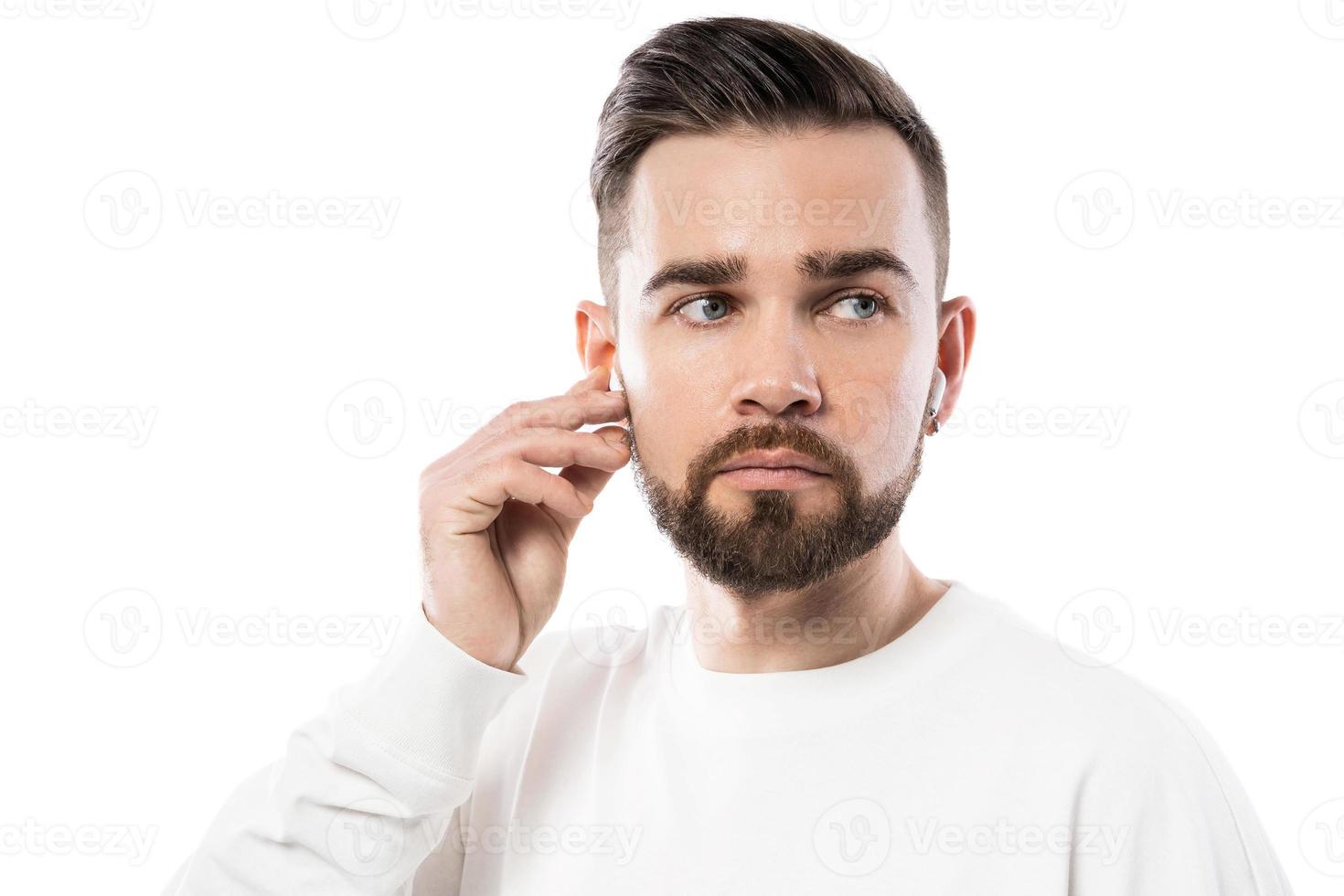 Handsome bearded man in white clothes  using wireless earbuds on white background photo