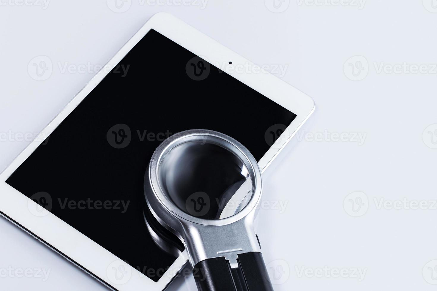 Closeup of magnifying glass and tablet computer photo