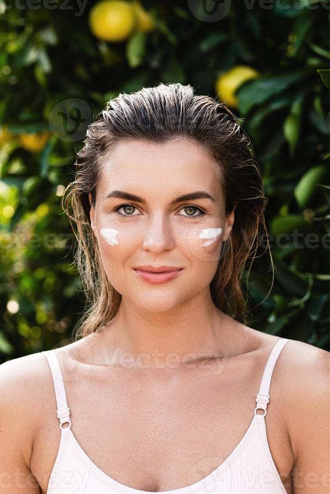 Beautiful woman with moisturizing cream under her eyes photo