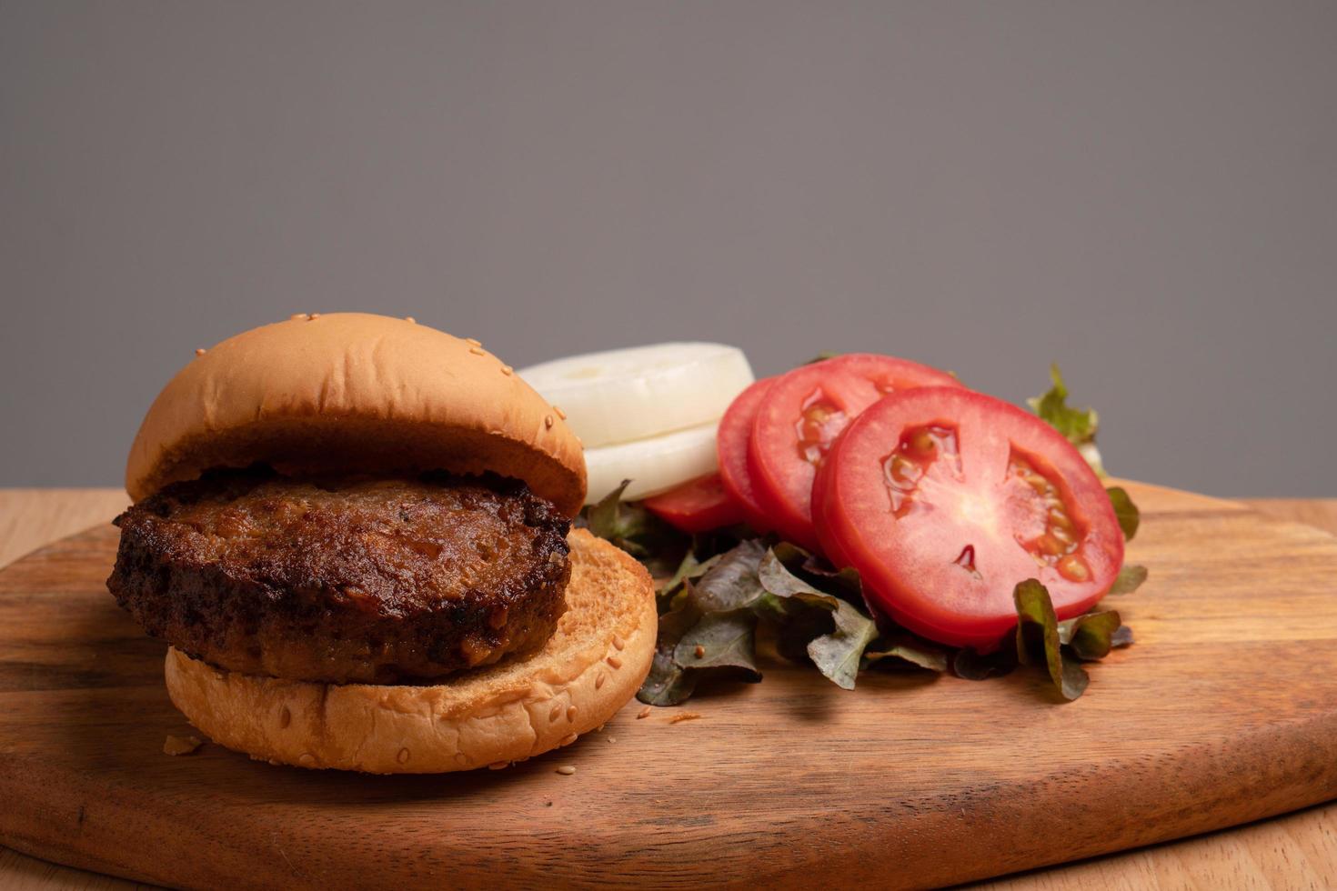 fresh tasty homemade hamburger with fresh vegetables, lettuce, tomato, cheese beside sliced tomatoes on a cutting board. Free space for text photo