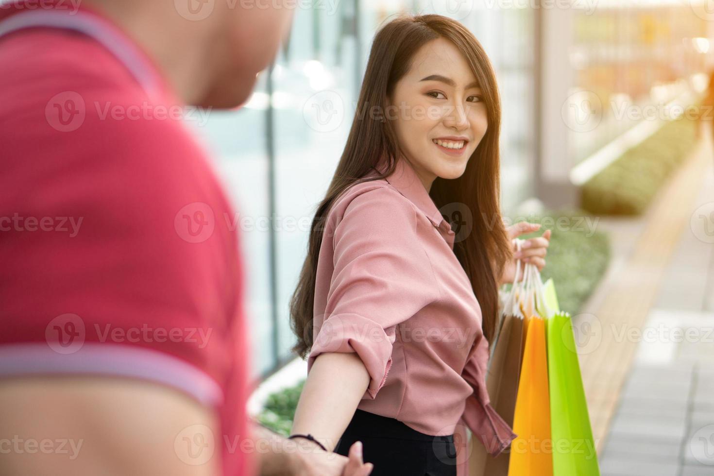 Happy young couple of shoppers walking in the shopping street towards and holding colorful shopping bags in hand. The woman turned and smiled at the man. Concept of sale and Black Friday shopping photo