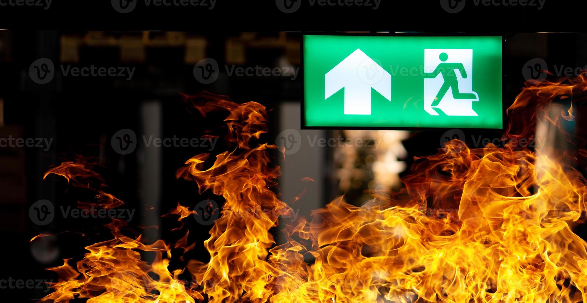 Hot flame fire and green fire escape sign hang on the ceiling in the Warehouse at night. The concept of fire escape training and preparation for evacuation photo