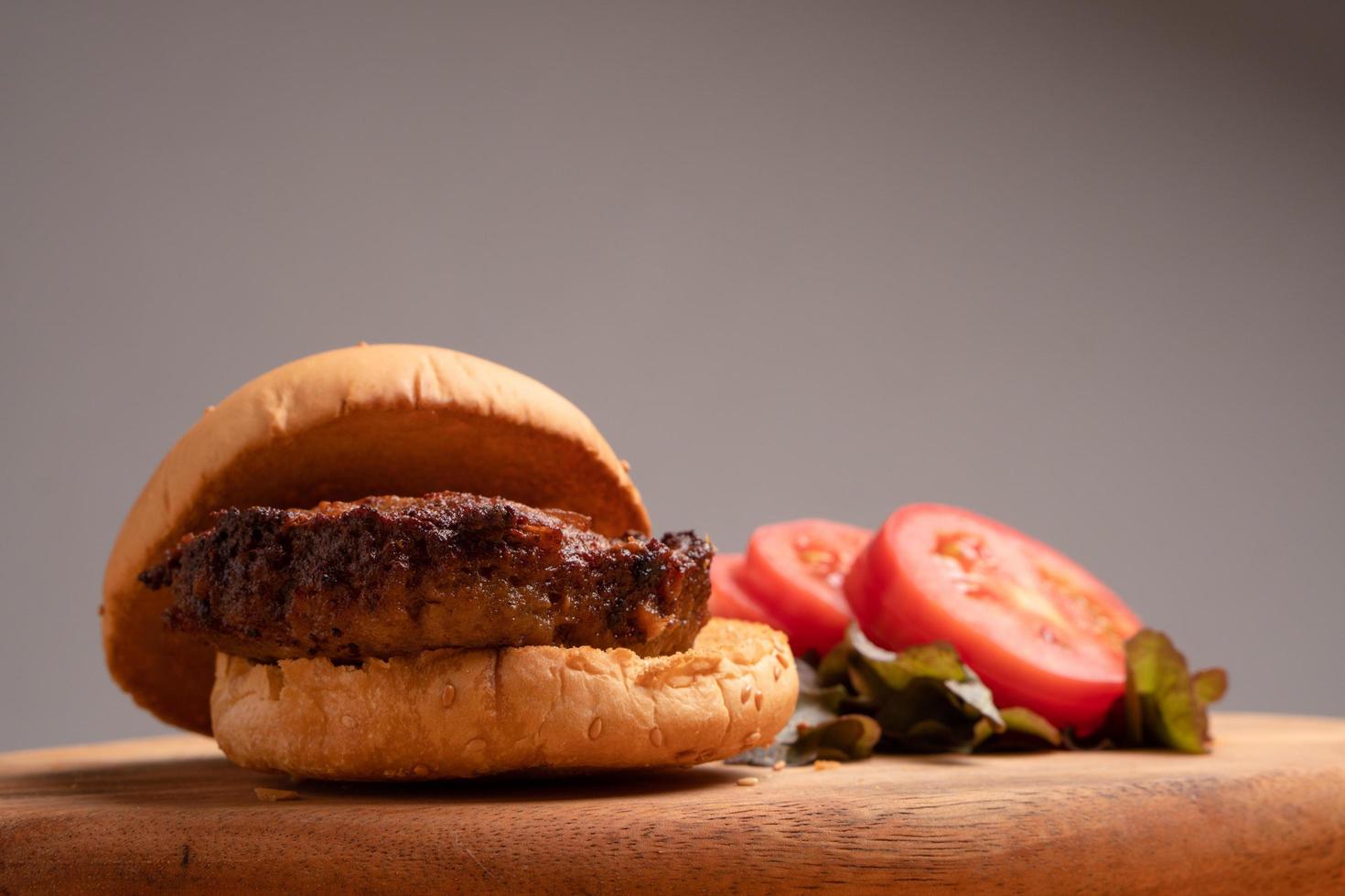 hamburguesa casera fresca y sabrosa con verduras frescas, lechuga, tomate, queso junto a rodajas de tomate en una tabla para cortar. espacio libre para texto foto