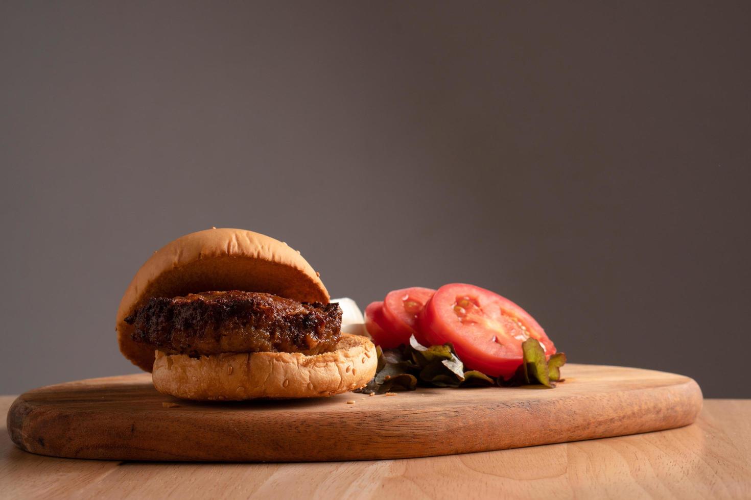 fresh tasty homemade hamburger with fresh vegetables, lettuce, tomato, cheese beside sliced tomatoes on a cutting board. Free space for text photo