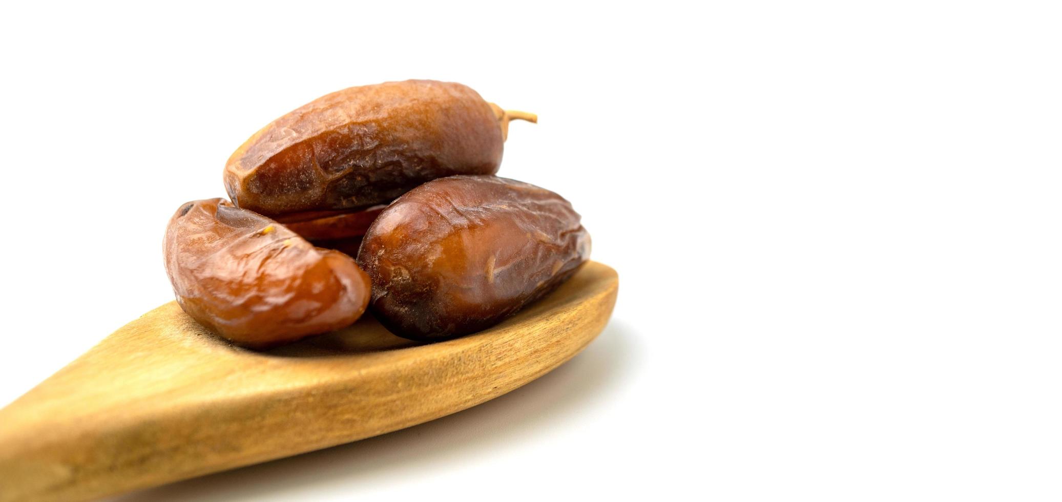 Dried of sweet dates palm fruits on wooden spoon on white background. Dates is a dried fruit that provides high energy. photo