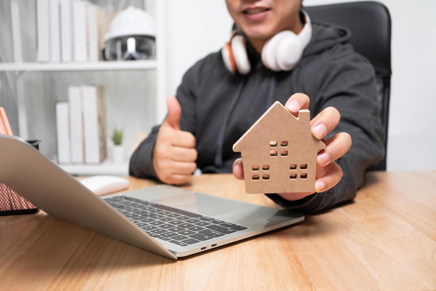 Smiling businessman holding a wooden house in home workspace. The concept of working from home until the end of Coronavirus COVID-19 quarantine, happily freelance working lifestyle photo