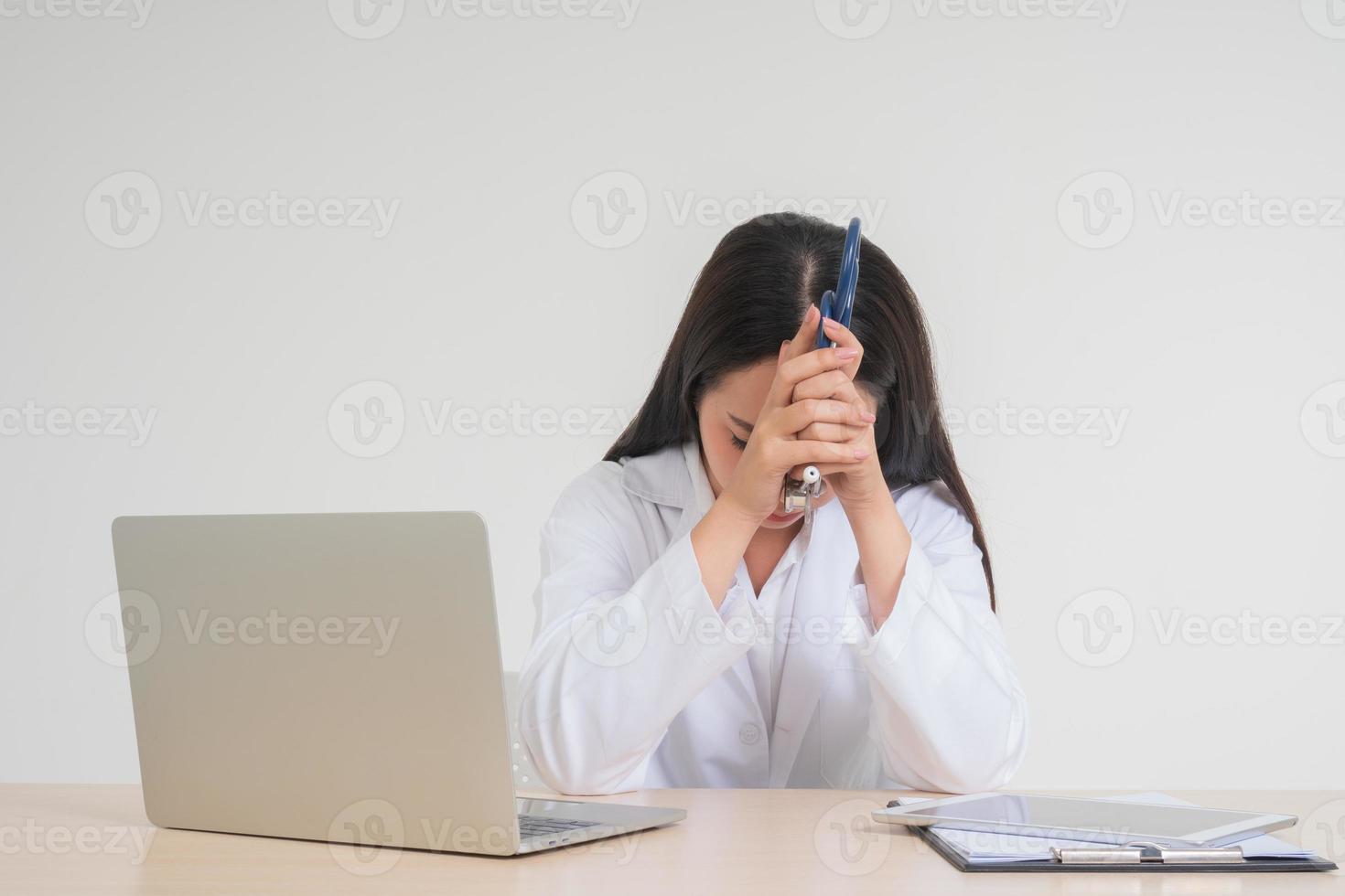 Young Asian woman doctor sitting on desk, she look unhappy and tired because of overwork, Concept of stressed exhausted and doctor liability, Dealing with frustrated photo