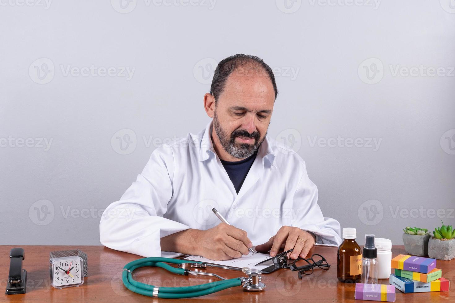 Portrait of senior mature doctor, pleasant professional in white coat sitting at table photo