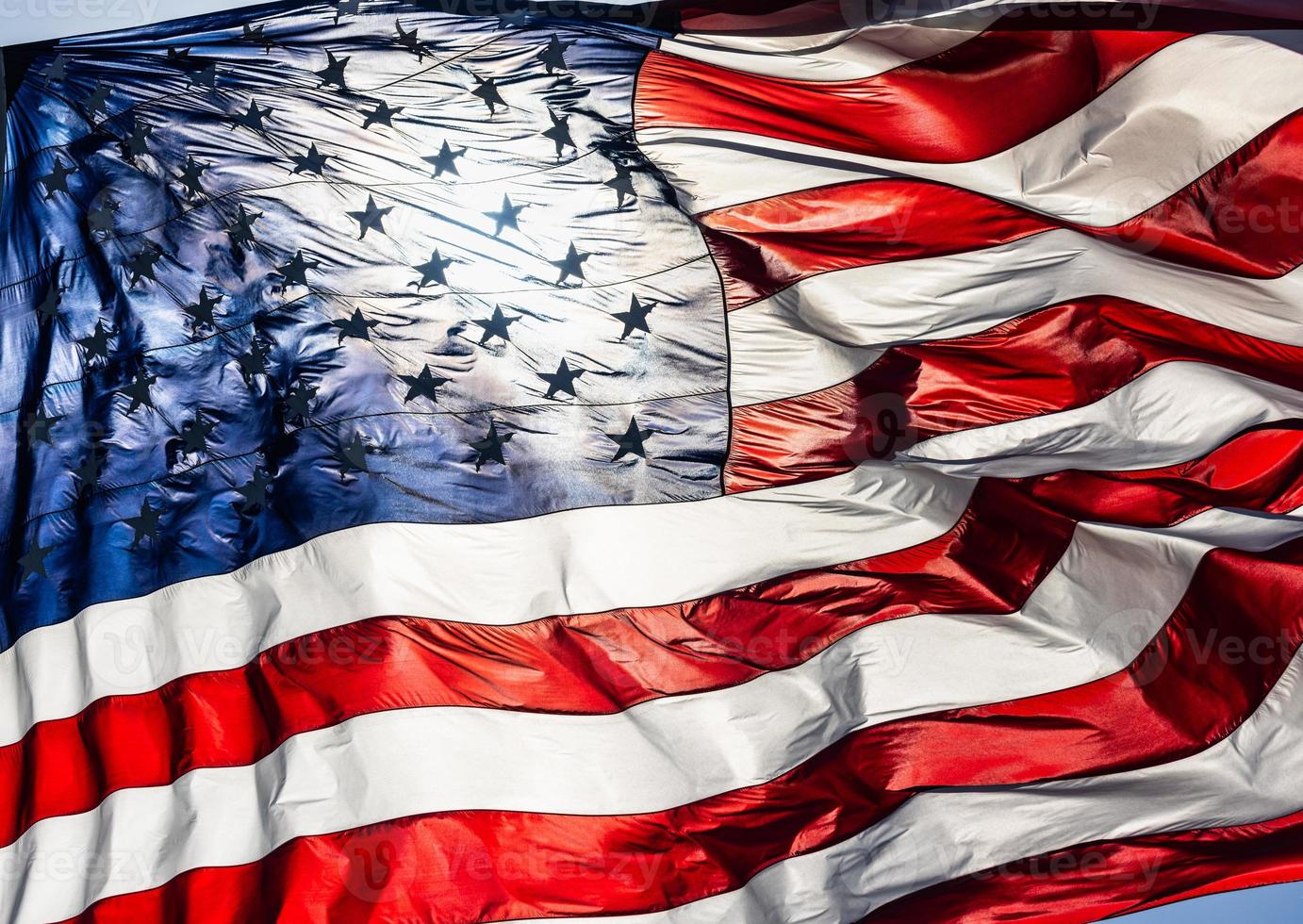Backlit American Flag Waving In Wind Against a Deep Blue Sky. photo
