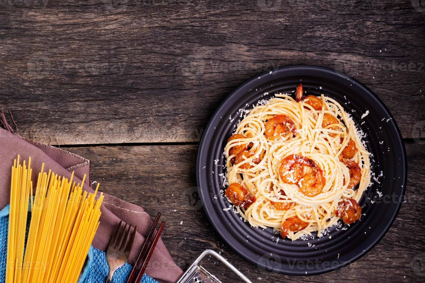 Delicious spaghetti pasta with prawns and cheese served in a black bowl on a black background table Italian recipe, tomato sauce, vegetables, and spices top view with copy space photo