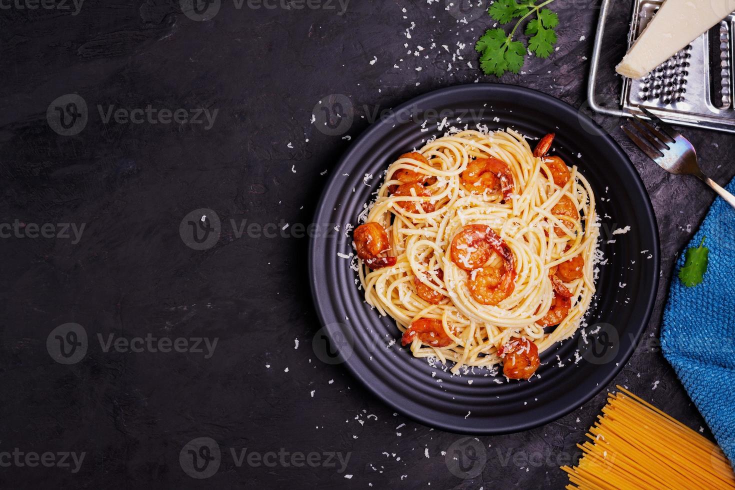 Delicious spaghetti pasta with prawns and cheese served in a black bowl on a black background table Italian recipe, tomato sauce, vegetables, and spices top view with copy space photo