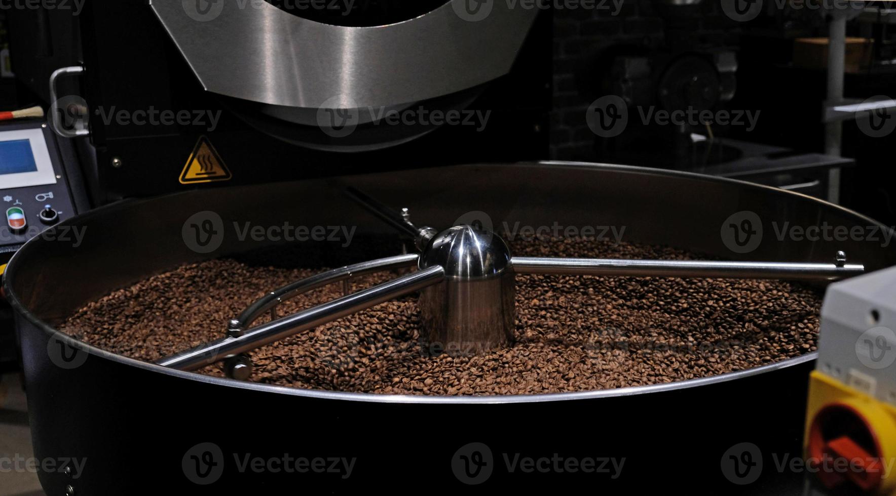 Coffee roaster machine at coffee roasting process. Mixing coffee beans. Roasted spinning cooler professional machines and fresh brown coffee beans movement close-up dark photo at factory.