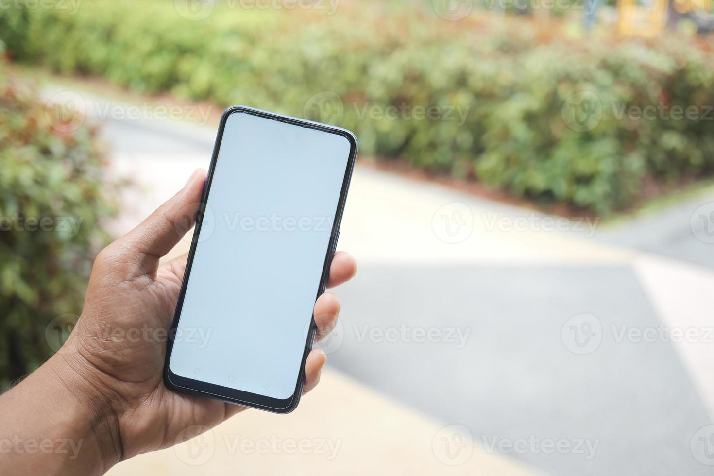 mano de hombre joven usando un teléfono inteligente con pantalla verde contra edificios de la ciudad foto