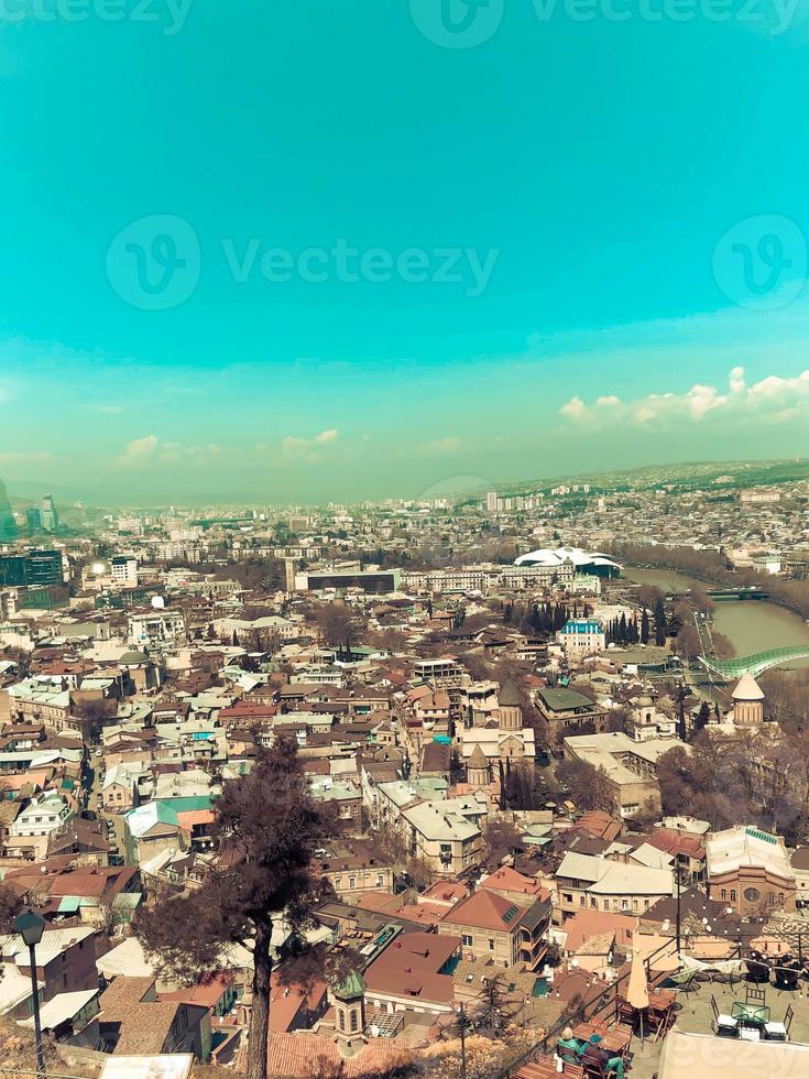 Vertical view from the top from a height of a beautiful tourist city with buildings and houses, roofs of trees and plants, nature against the blue sky and mountains. European old architecture photo