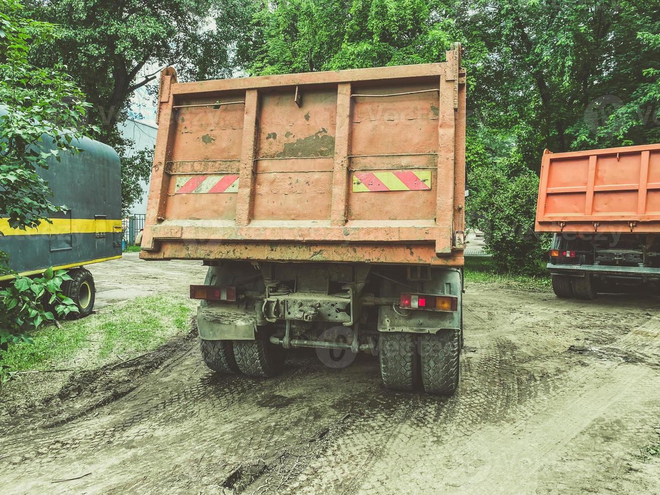 a huge truck with a body for transporting heavy things. heavy-duty vehicle sticker on the back of the body. the car is driving on a dirty, wet road photo
