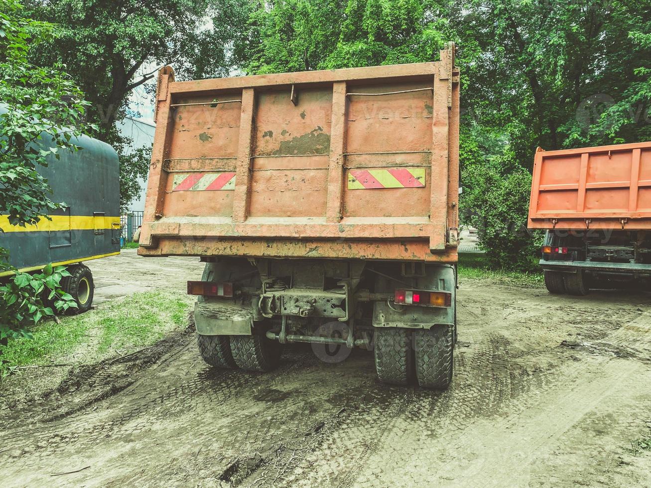 un enorme camión con carrocería para transportar cosas pesadas. pegatina de vehículo pesado en la parte trasera de la carrocería. el coche conduce por una carretera sucia y mojada foto