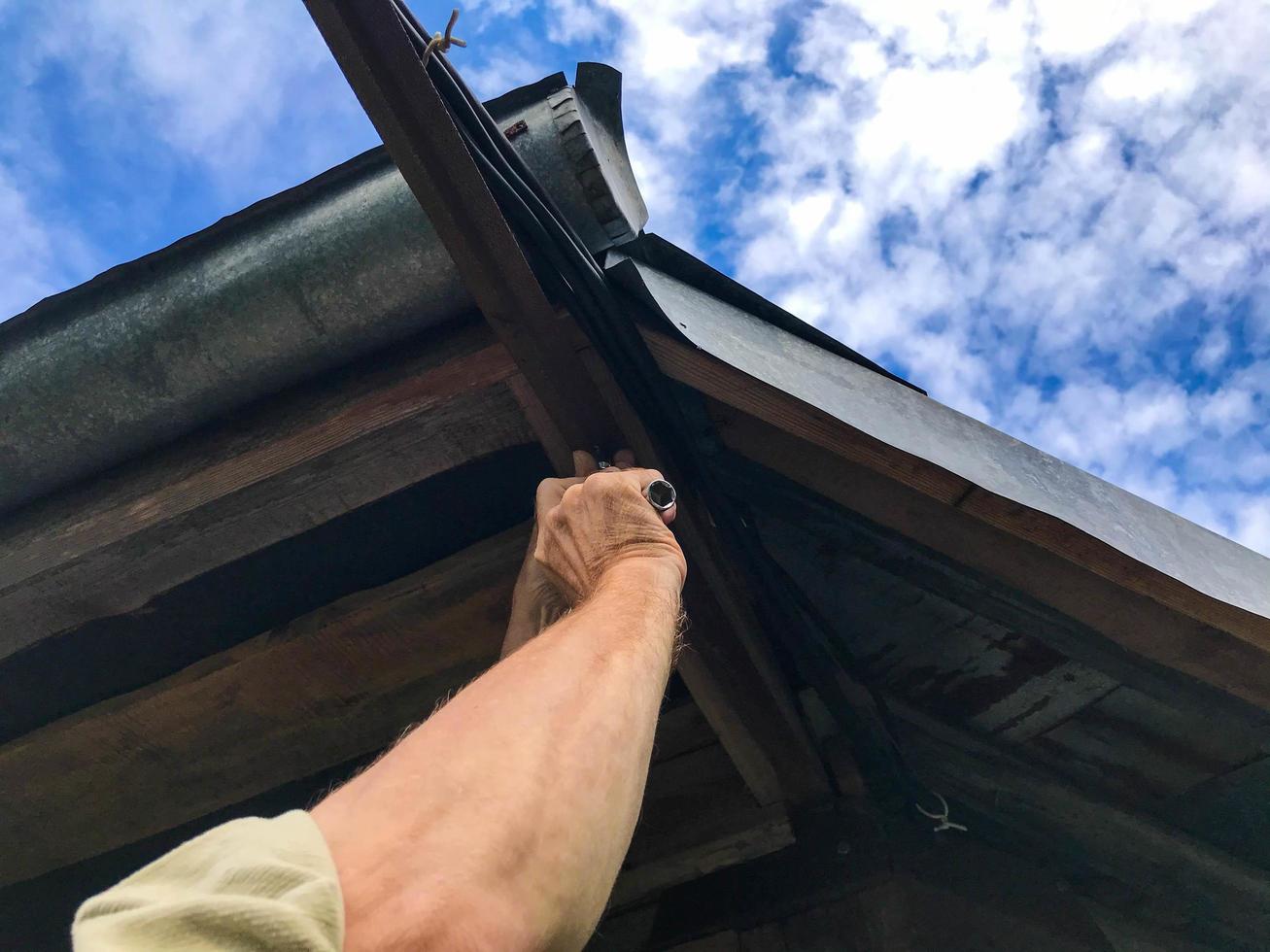 man repairs the roof at a height. manufacturing  in a wooden house. sealing holes, holes in a residential building. roof fitter. repairs the roof with metal tools, tightens the bolts photo