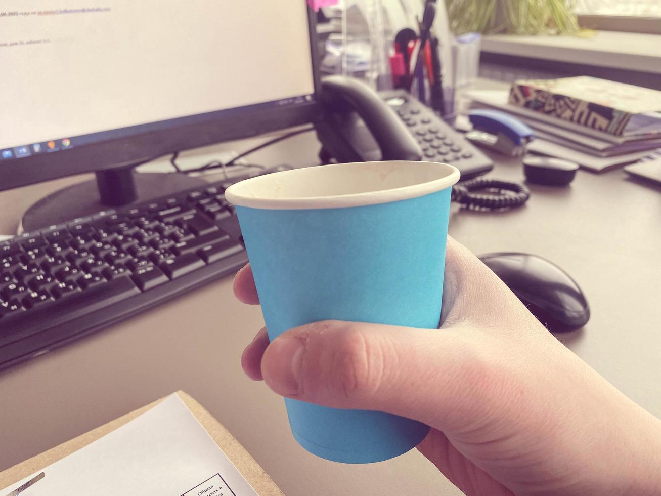 Cup of coffee, keyboard and desktop computer on desk in white home office interior. Real photo